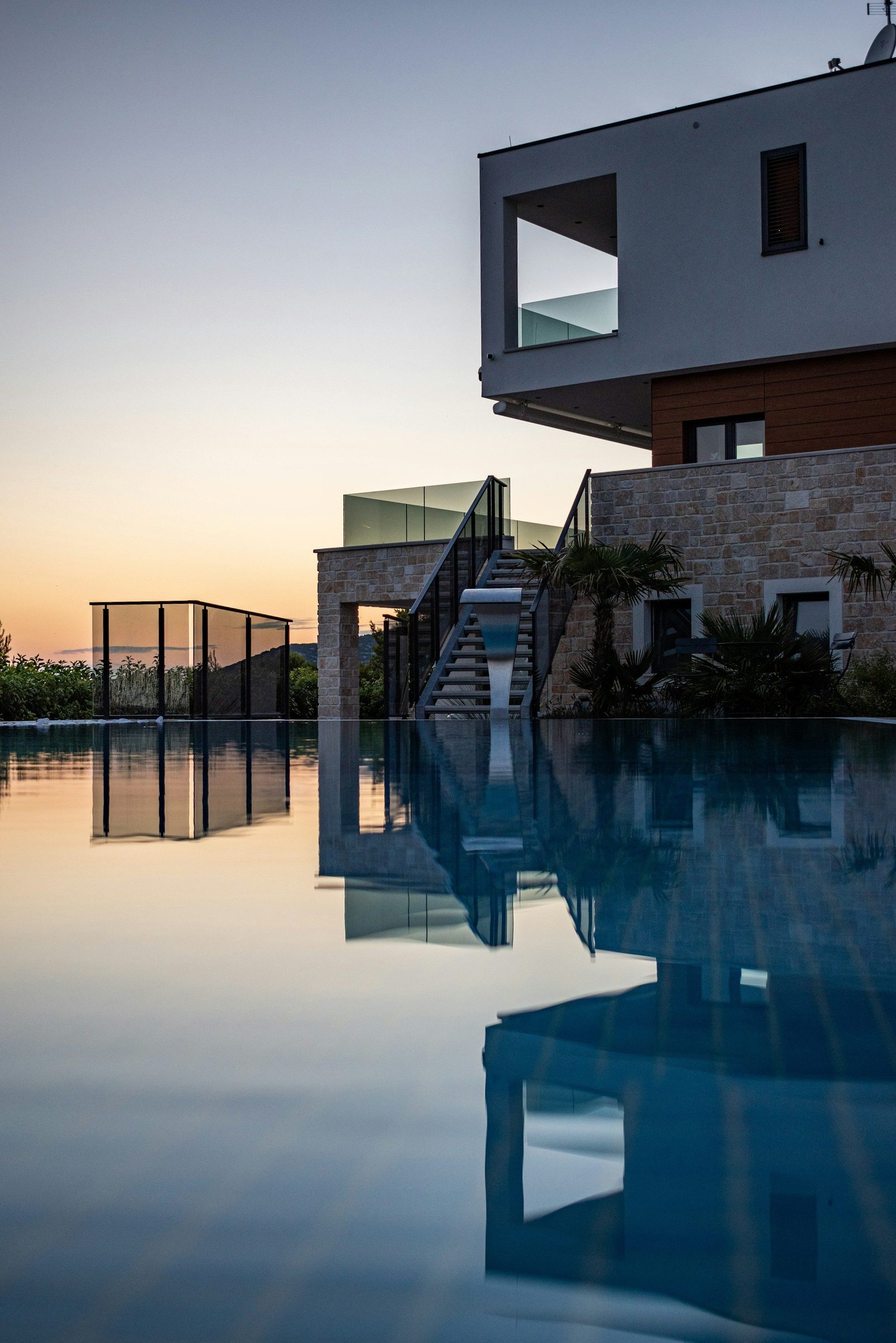 Piscina infinita a refletir a casa ao pôr do sol.