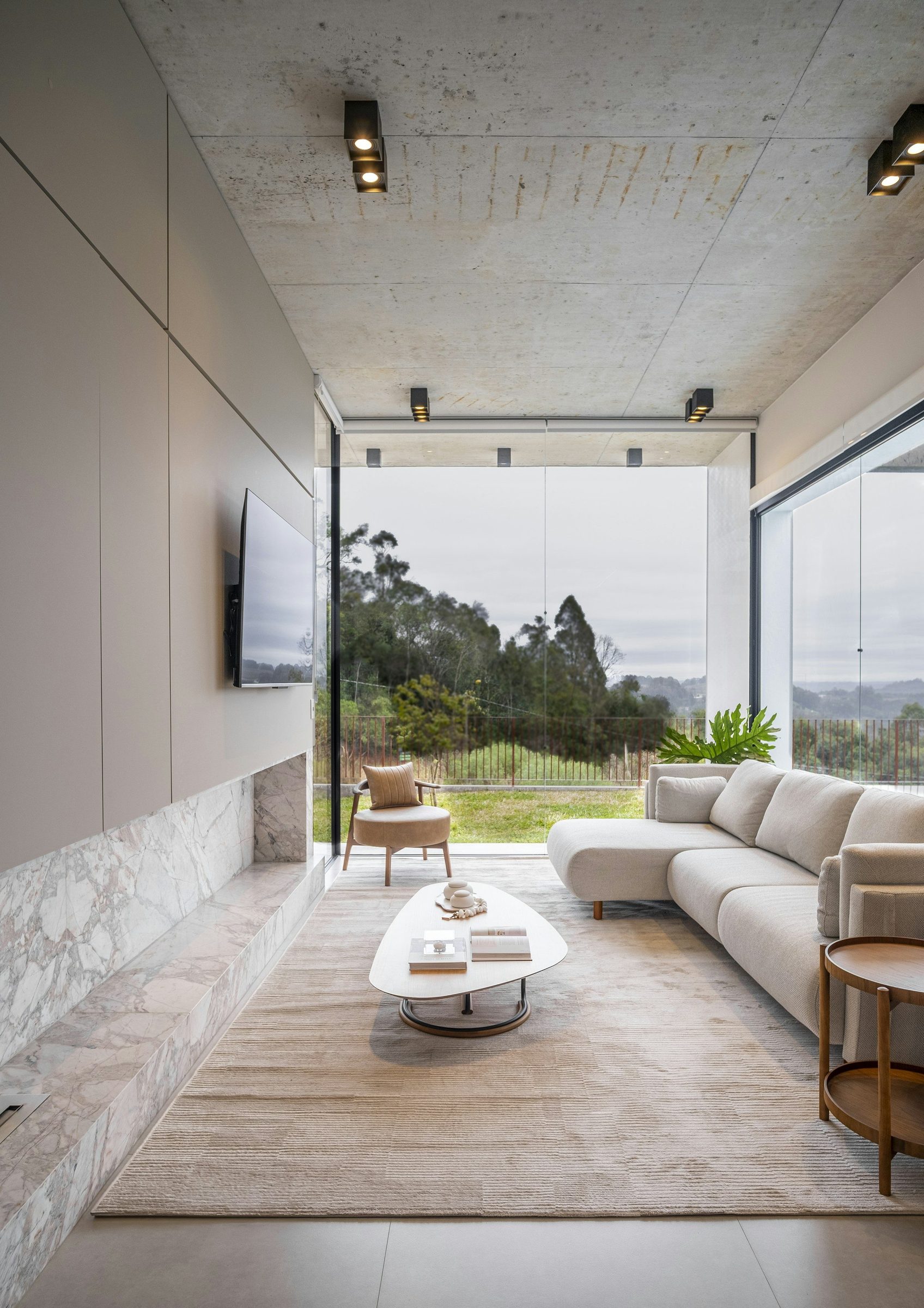 Sala minimalista com parede de vidro aberta para o jardim.