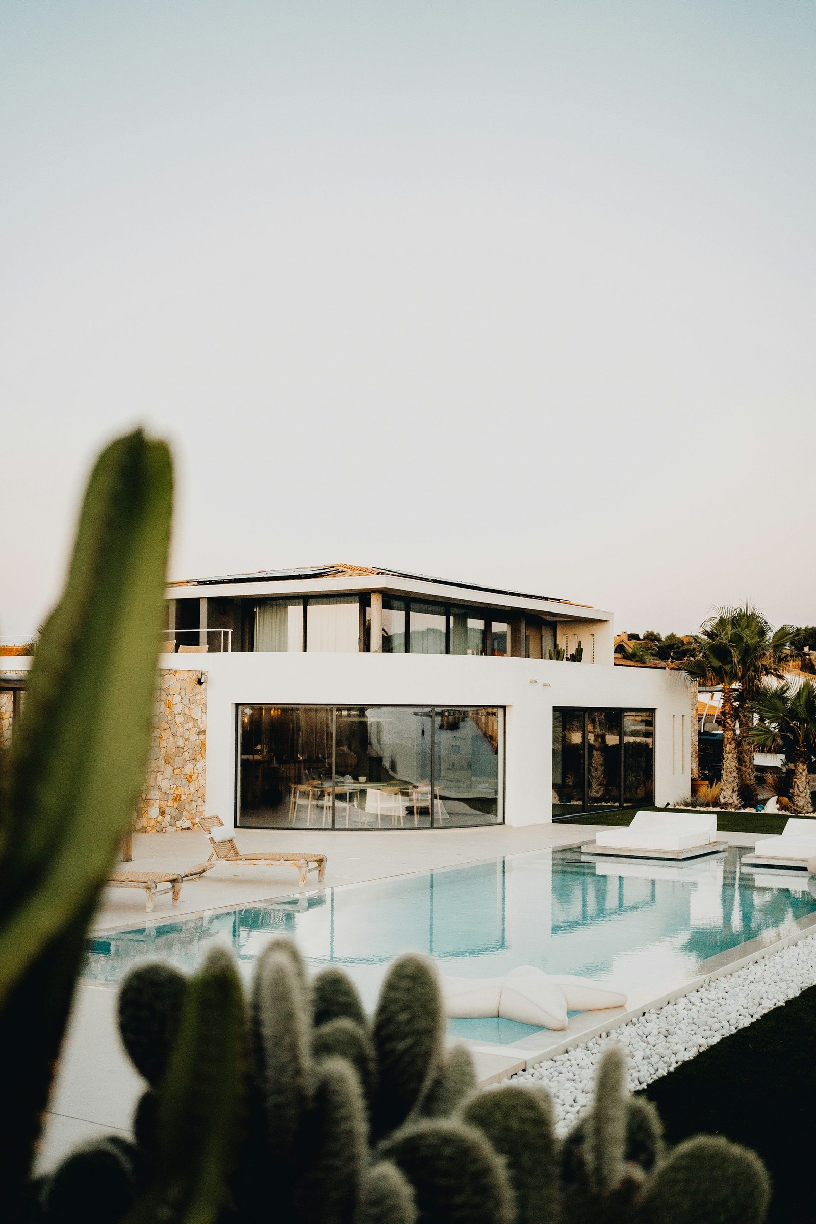 Moradia branca contemporânea com piscina e catos em primeiro plano.